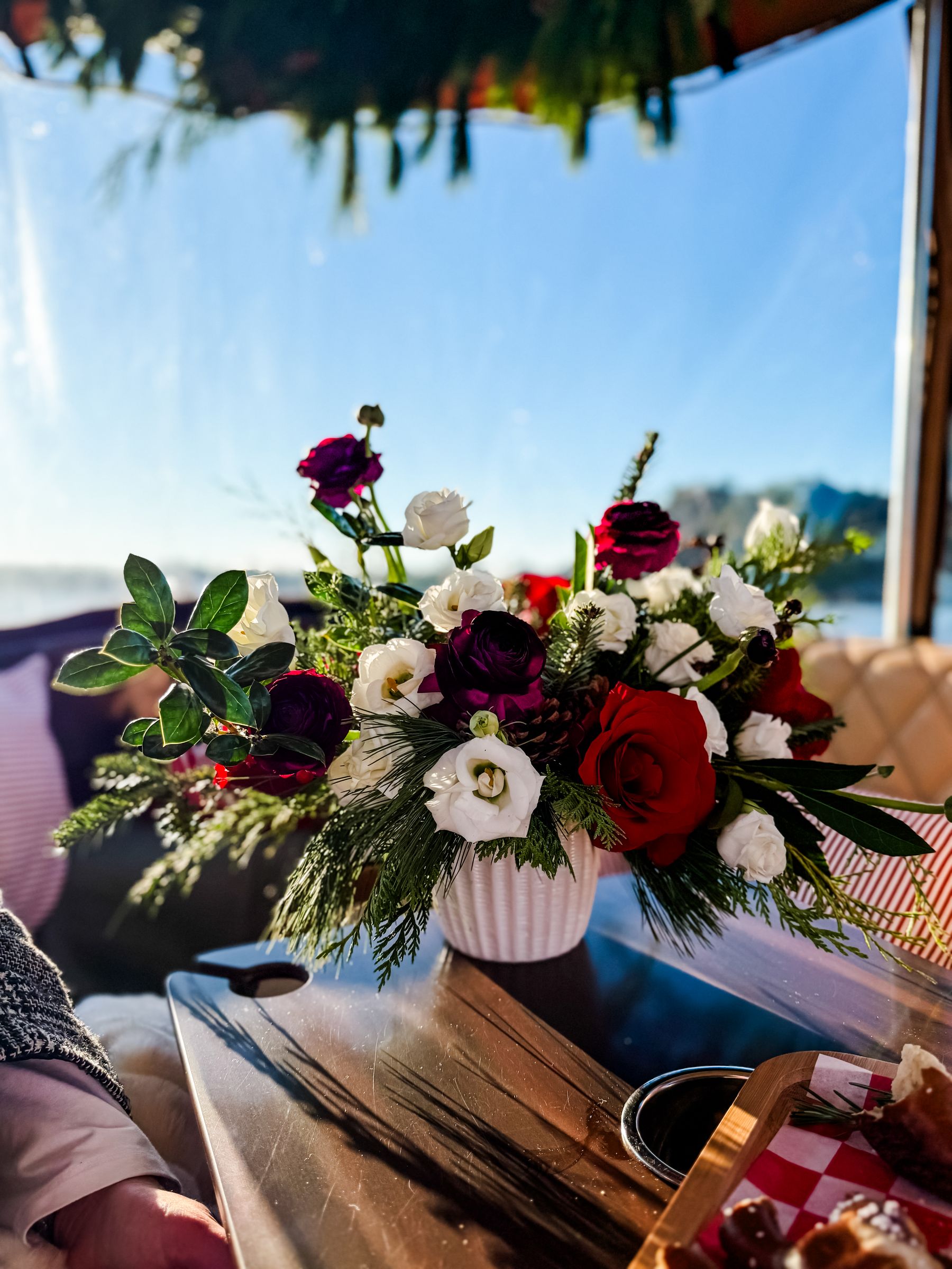 Ramona Studios holiday arrangement of red roses, white lisianthus and evergreens on the Joyride table