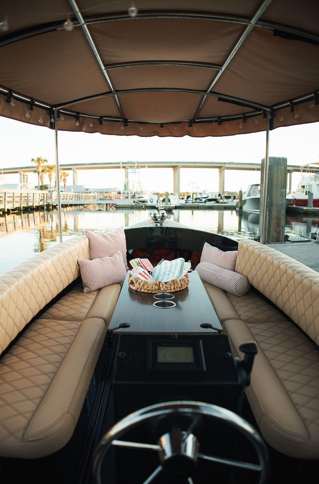 Inside the Joyride boat: quilted cream seating, striped pillows and a center table, looking past the helm toward the bridge