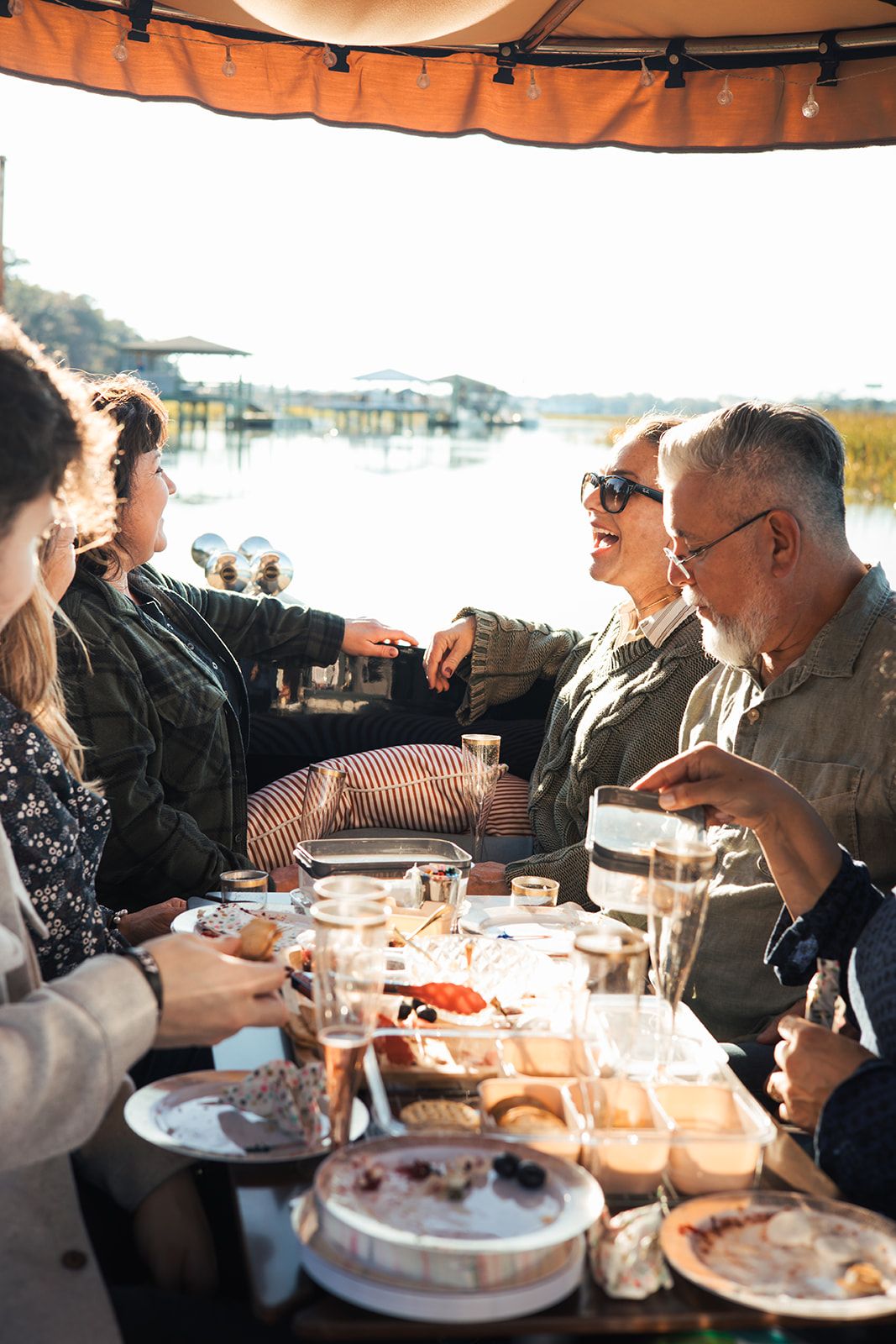 Friends laughing around the table on a private Joyride cruise, with the salt marsh behind them