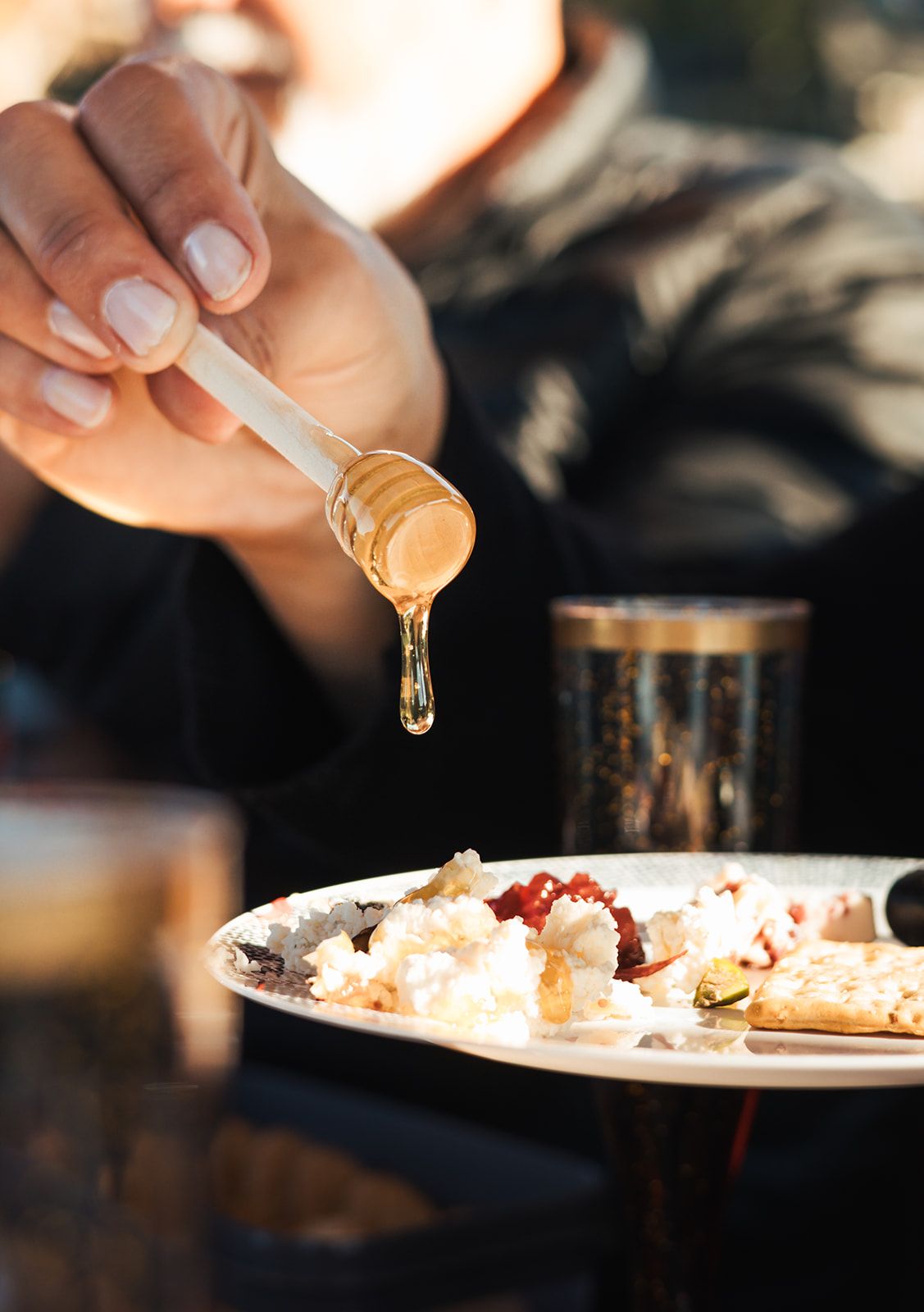 Honey drizzled over cheese beside a gold-rimmed glass on board