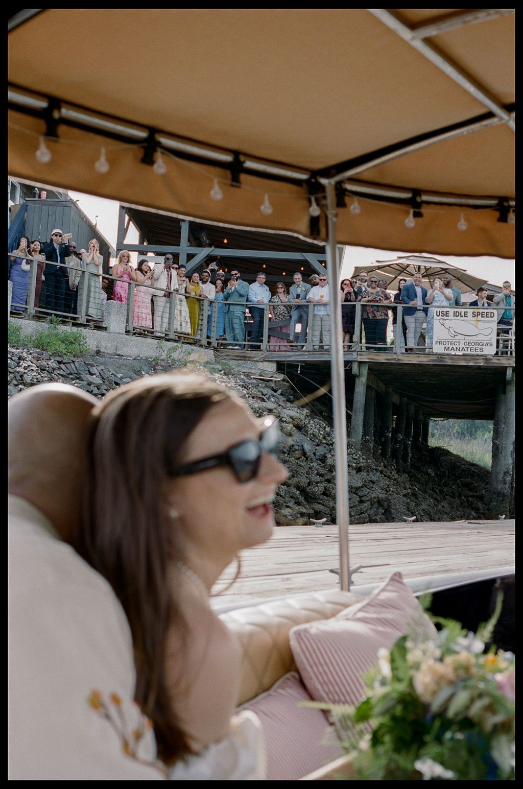 Wedding guests cheering from The Wyld's deck as the couple arrives by boat