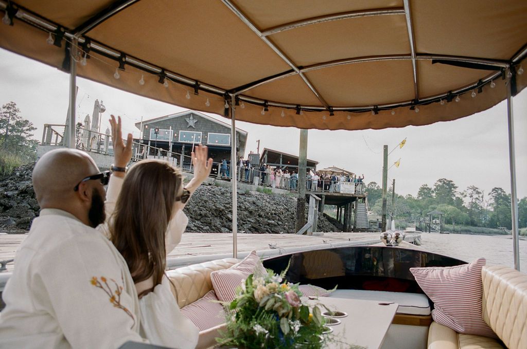 Newlyweds waving to cheering guests on The Wyld's deck as the Joyride boat pulls in