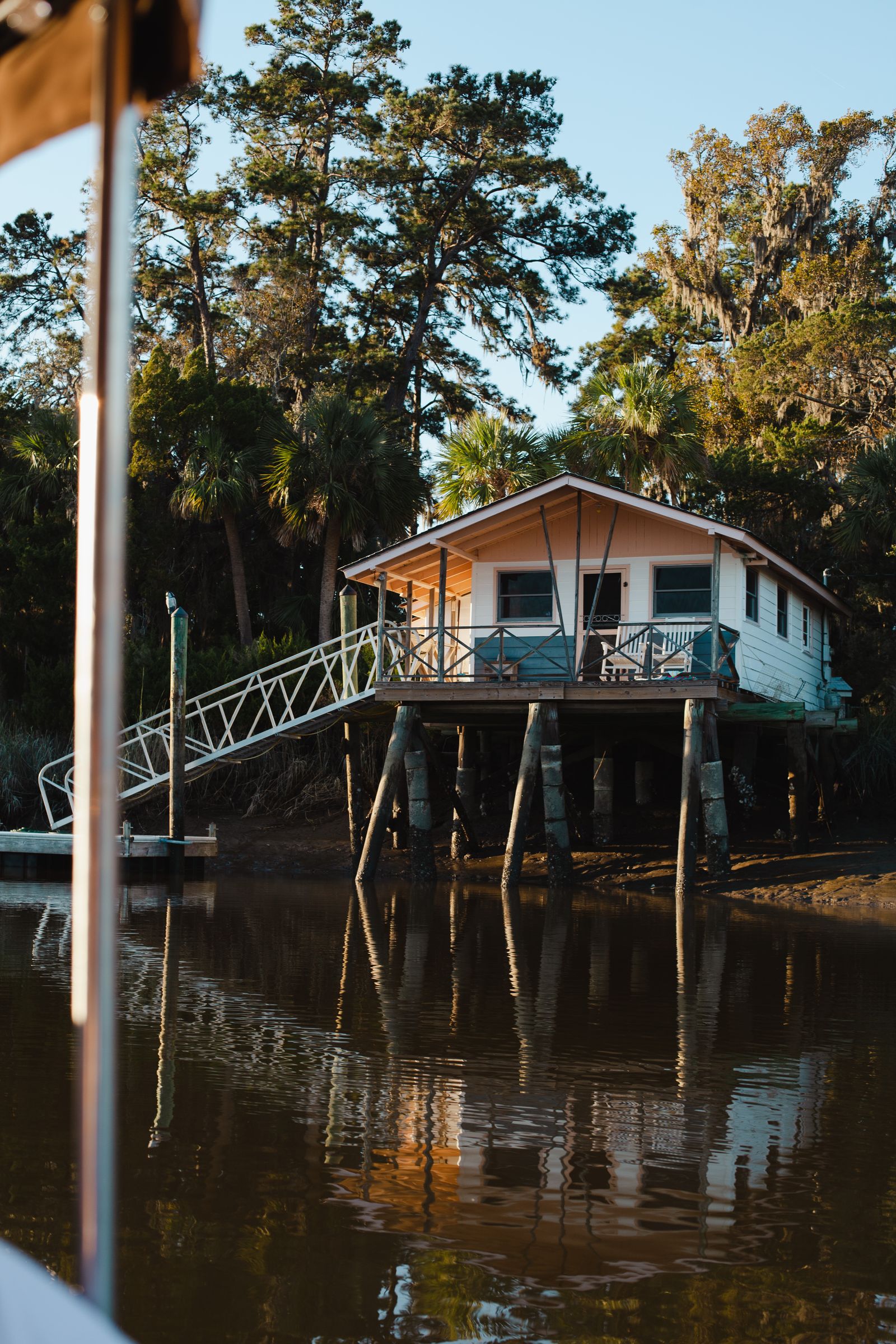 A pastel stilt house with a long dock and live oaks on the marsh