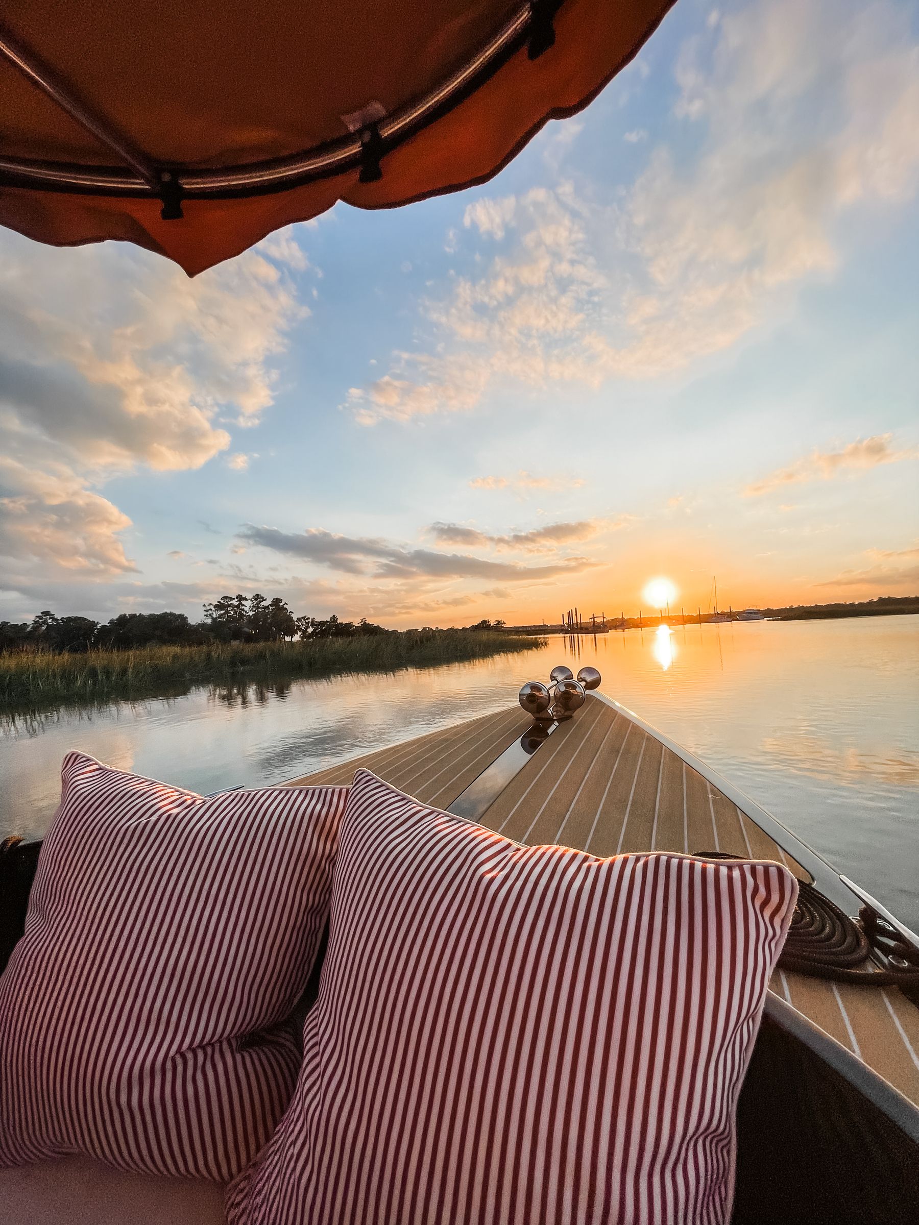 Sunset over the marsh from the Joyride bow, red-striped pillows and the canopy in the foreground