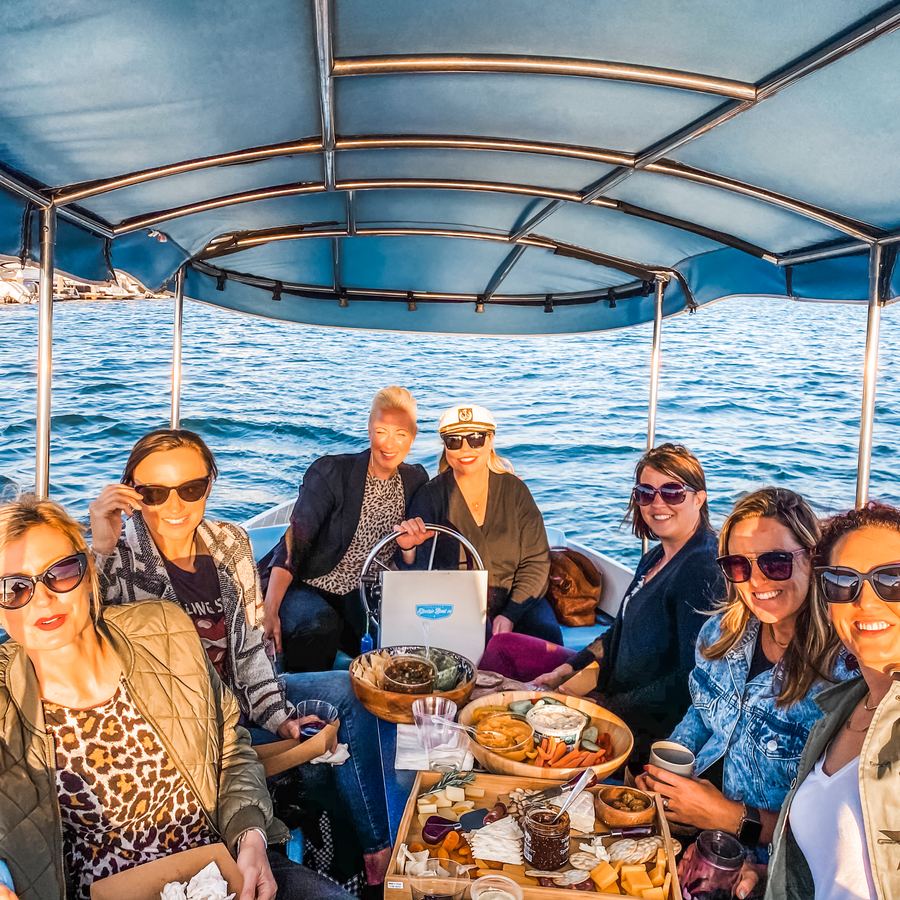 Audra and friends on a canopied electric boat in Newport Beach with a charcuterie spread