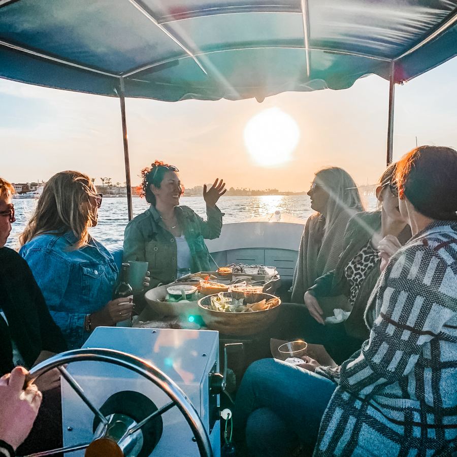 Friends gathered around the table on an electric boat at sunset in Newport Beach