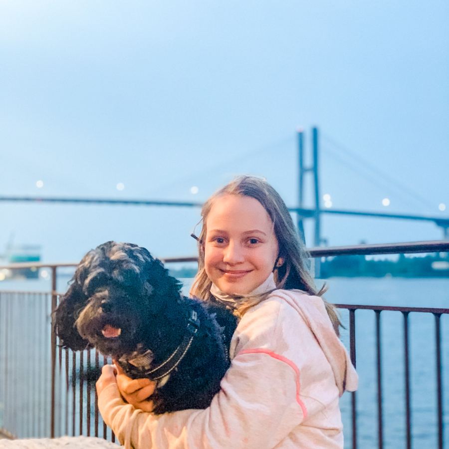 Audra's daughter hugging Zeus, the family's curly black pup, on River Street with the Talmadge Bridge behind