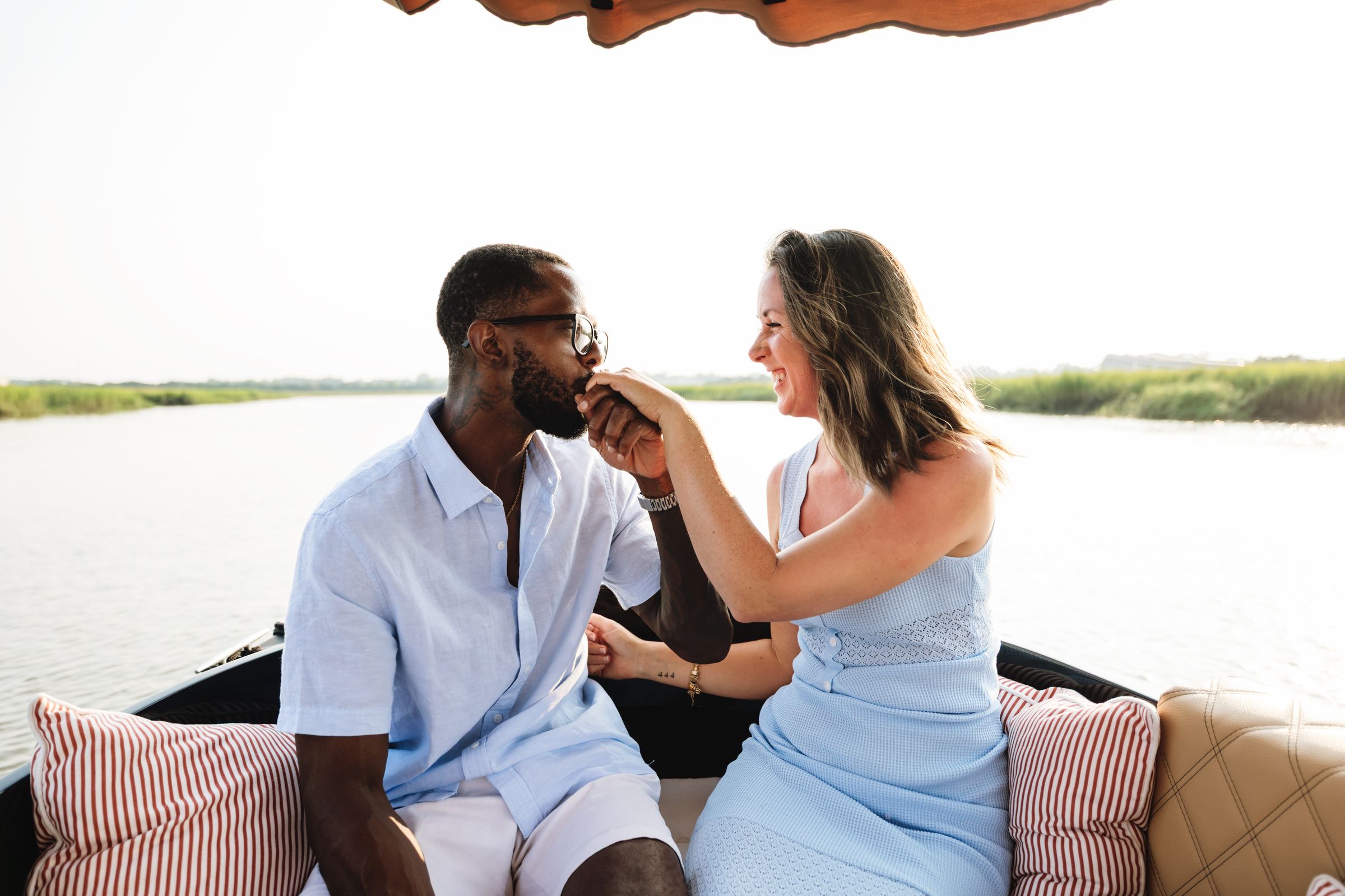 On the bow, he kisses her hand after the proposal, salt marsh all around