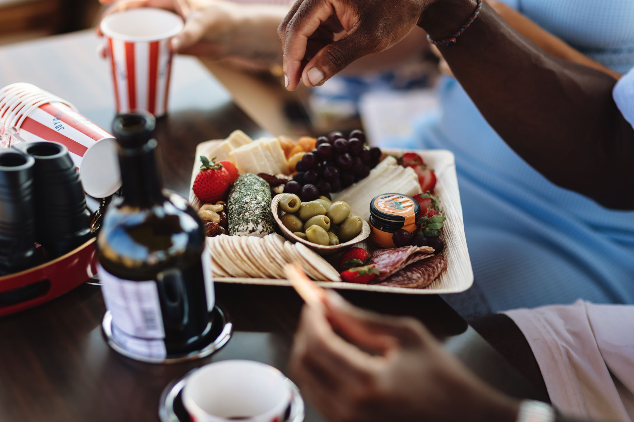 Guests reaching for a Provisions Savannah charcuterie board with wine and red-striped Joyride cups on board